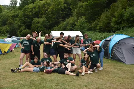 Die Gruppe der Mitarbeiter bei einer Rreizeit machen ein lustiges Gruppenbild vor den Zelten im Erdbeertal