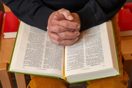 Gefaltete Hände über aufgeschlagener Bibel.